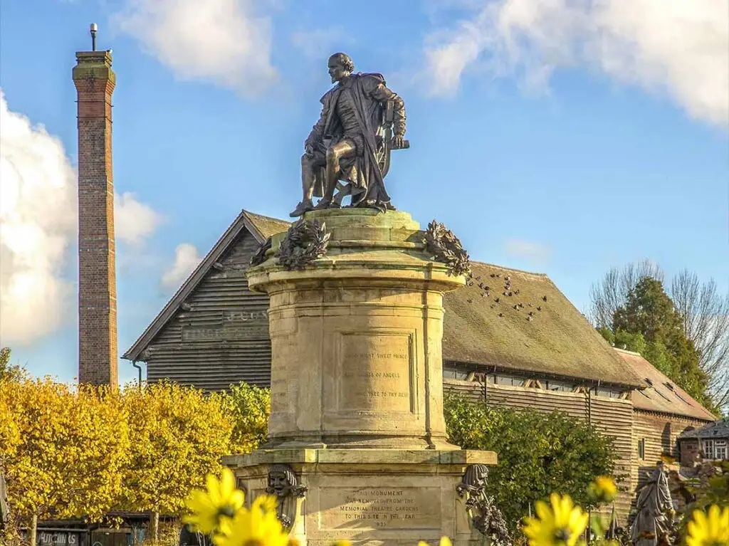 Statue of William Shakespeare in Stratford-upon-Avon, surrounded by vibrant yellow flowers and historic buildings, perfect for Luxe Tours exploring literary heritage.