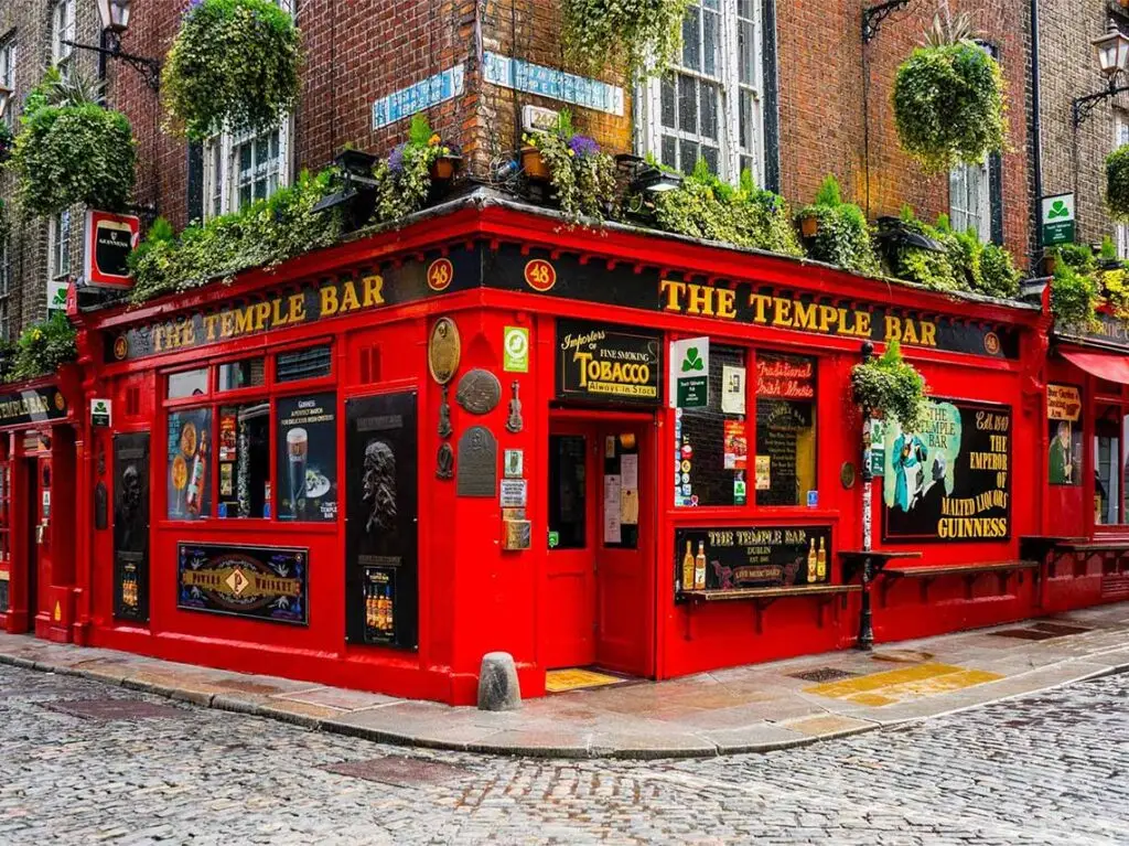 The iconic Temple Bar pub in Dublin, Ireland, showcasing its vibrant red facade and colorful decorations on a cobblestone street.