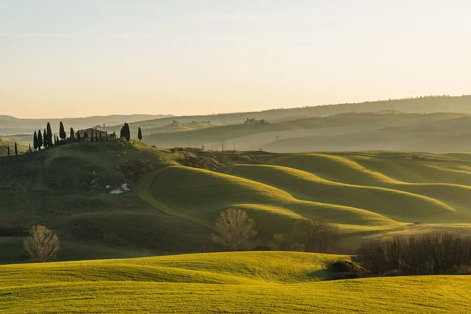 Scenic view of Val d'Orcia at sunrise with rolling hills and a traditional Tuscan farmhouse, Tuscany, Italy — ideal for luxe travel tours