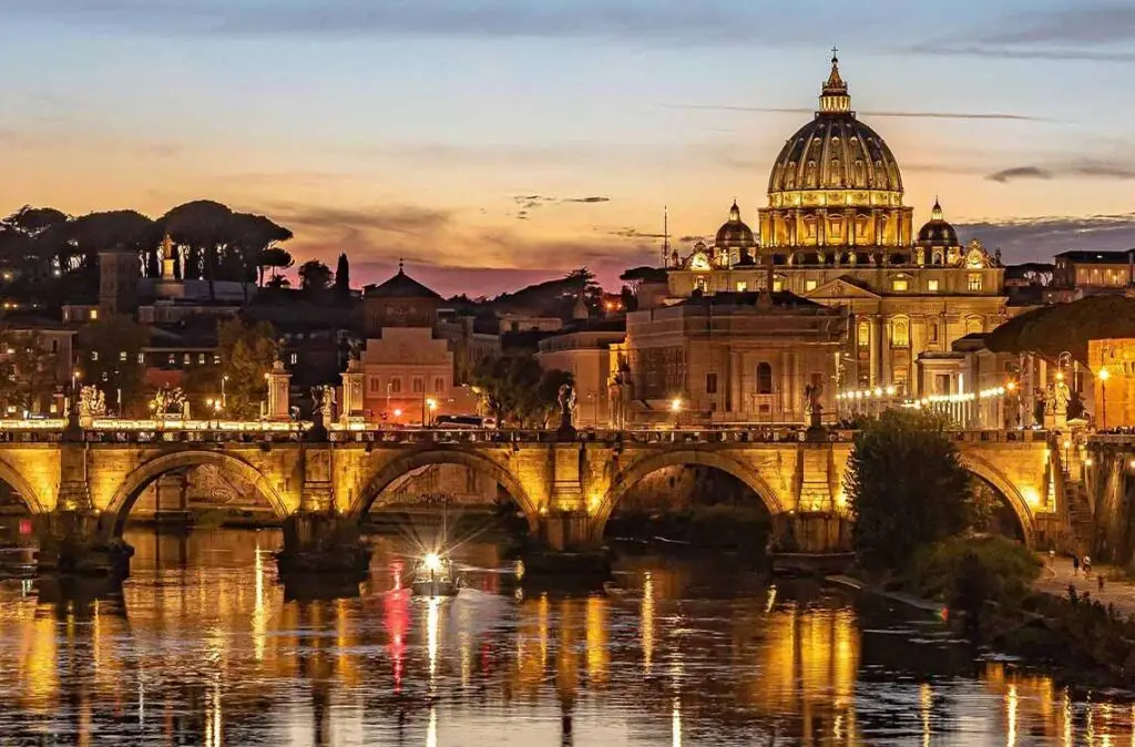 Illuminated view of St. Peter's Basilica and Ponte Sant'Angelo over the Tiber River at night in Vatican City.