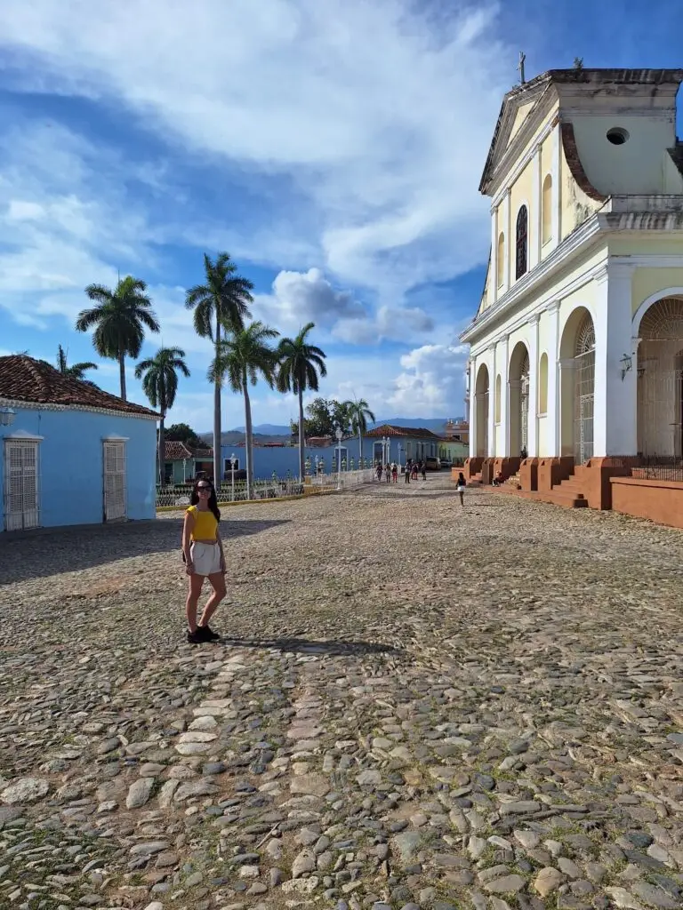 Tourist exploring the cobblestone streets of Vittoria with historic church and palm trees in the background, sunny day in Europe.