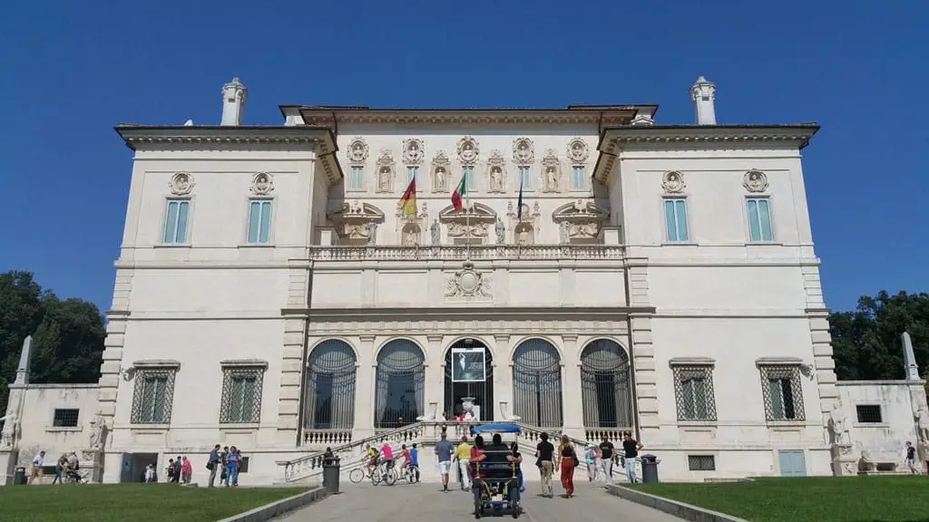 Exterior view of Galleria Borghese in Rome, showcasing tourists exploring the iconic Italian art museum on a sunny day.