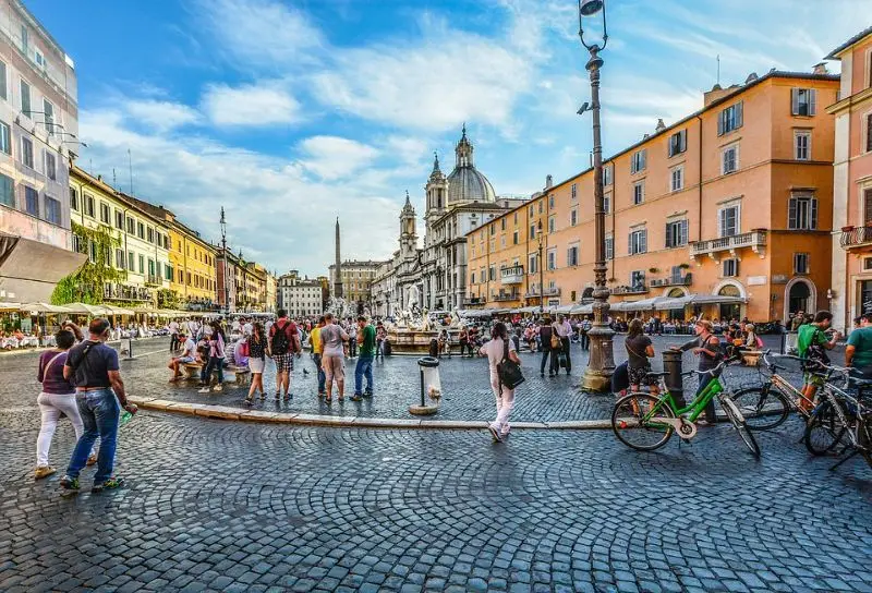 Vibrant street view of Piazza Navona in Rome with tourists enjoying the famous fountains and baroque architecture on a sunny day.