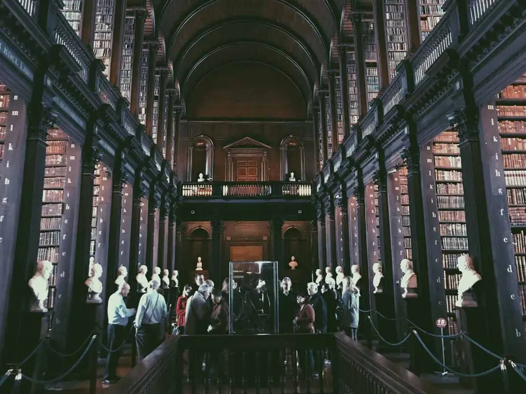 Visitors touring the historic Long Room in the Old Library at Trinity College Dublin, showcasing rows of ancient books and the richly embellished wooden architecture