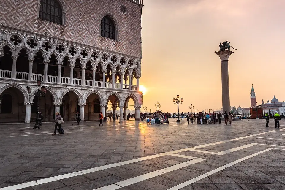 Sunset view of Piazza San Marco with Doge's Palace and the Column of San Marco, Venice, Italy, showcasing Venetian architecture and bustling tourism.