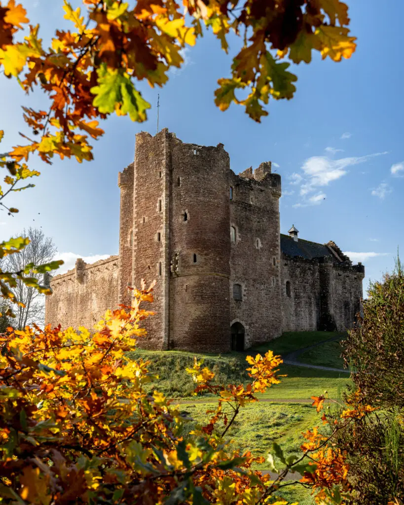 Doune Castle in Scotland framed by colorful autumn leaves, a famous filming location for Monty Python, Game of Thrones, and Outlander set in a scenic natural backdrop.